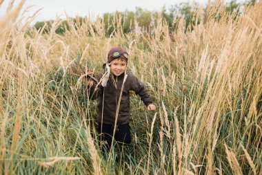 Bir çocuk kırmızı bir uçak ile oynuyor. Çocuk uzun otların bir alana