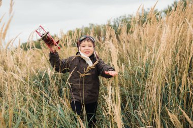 Bir çocuk kırmızı bir uçak ile oynuyor. Çocuk uzun otların bir alana