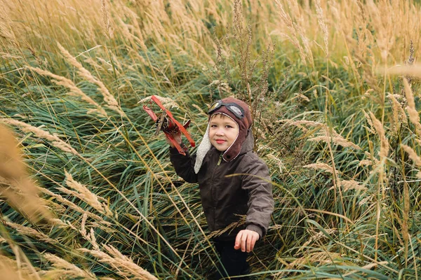 Bir çocuk kırmızı bir uçak ile oynuyor. Çocuk uzun otların bir alana