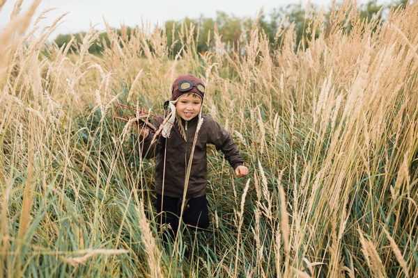 Bir çocuk kırmızı bir uçak ile oynuyor. Çocuk uzun otların bir alana