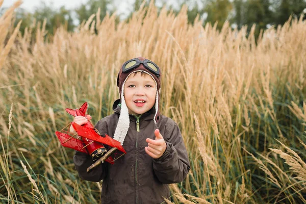 Bir çocuk kırmızı bir uçak ile oynuyor. Çocuk uzun otların bir alana