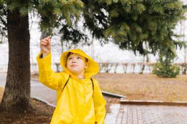 Bir gr bir kolu çekerek bir kukuleta ile sarı bir pelerin içinde mutlu çocuk
