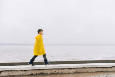 Sarı pelerin (yağmurluk) çocukta kıyı yürüyor. G