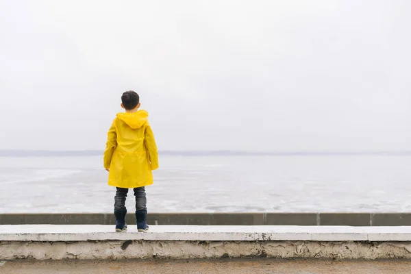 Sarı bir pelerin içinde bir oğlan su görünümünü hayran. Bac olduğunu