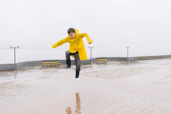 黄色のレインコートを水たまりにジャンプで幸せな少年. — ストック写真