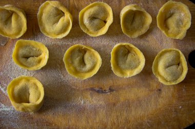 Freshly prepared Italian tortellini on wooden board top view clipart