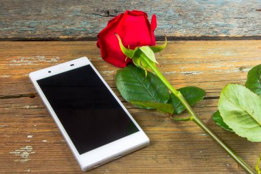 Smartphone ve eski ahşap bir masa üzerinde kırmızı gül