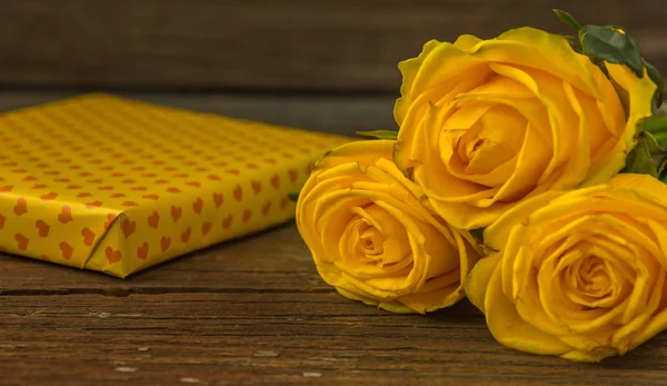 Gele rozen en de doos van de gift op een oud houten tafel — Stockfoto