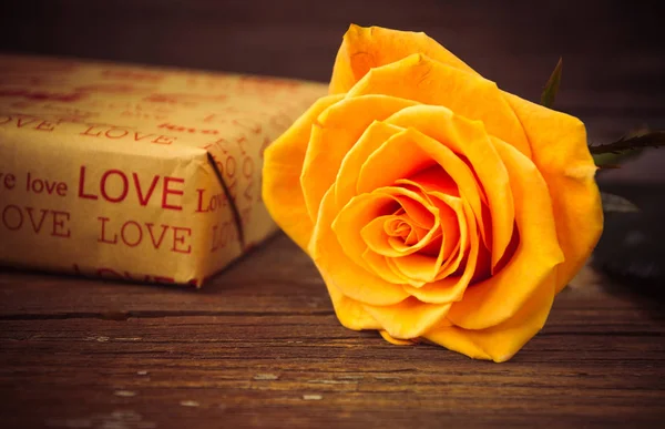 Rosa amarilla y caja de regalo en una vieja mesa de madera — Foto de Stock