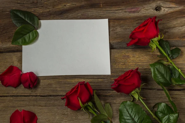 Rote Rosen und weißes leeres Papier auf hölzernem Hintergrund, Draufsicht Stockfoto