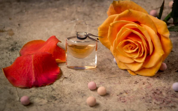 Perfume en una botella de vidrio y flor de rosa naranja — Foto de Stock