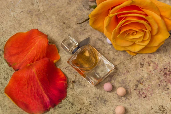 Perfume en una botella de vidrio y flor de rosa naranja — Foto de Stock
