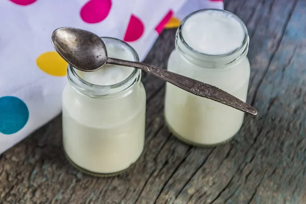 Sklenice s bílým jogurtem a lžičkou na dřevěné pozadí — Stock fotografie