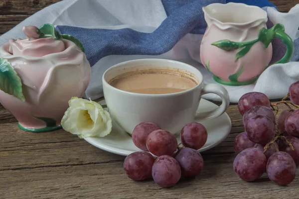 Чашка кави з молоком, червоним виноградом, рожевим посудом та еустомами — стокове фото