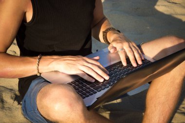 Genç adam sahilde dizüstü bilgisayar üzerinde çalışıyoruz. Ucu