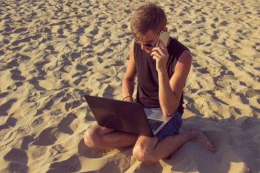 Dizüstü bilgisayar ve cep telefonu sahilde olan genç adam. Yapmak
