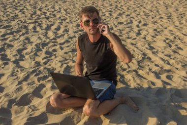 Dizüstü bilgisayar ve cep telefonu sahilde olan genç adam. Yapmak