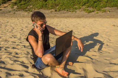 Dizüstü bilgisayar ve cep telefonu sahilde olan genç adam. Yapmak