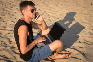 Dizüstü bilgisayar ve cep telefonu sahilde olan genç adam. Yapmak