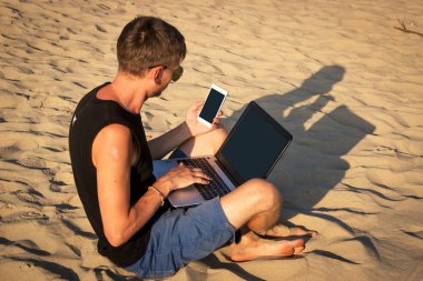 Dizüstü bilgisayar ve cep telefonu sahilde olan genç adam. Yapmak