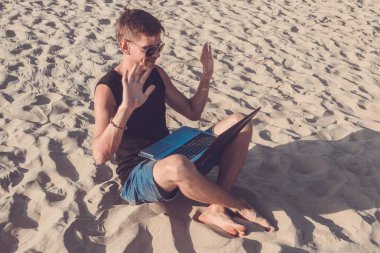 Genç adam sahilde dizüstü bilgisayar üzerinde çalışıyoruz. Ucu