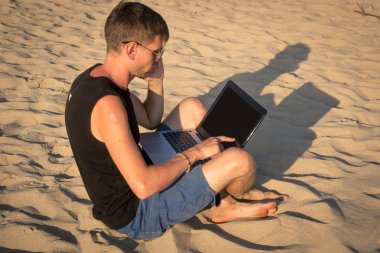 Dizüstü bilgisayar ve cep telefonu sahilde olan genç adam. Yapmak