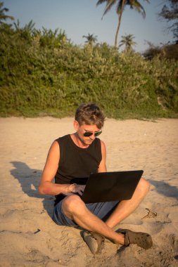 Genç adam sahilde dizüstü bilgisayar üzerinde çalışıyoruz. Ucu