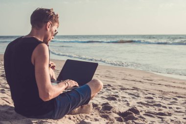 Genç adam sahilde dizüstü bilgisayar üzerinde çalışıyoruz. Ucu