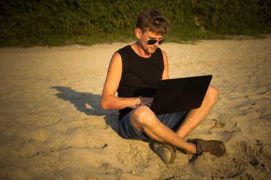 Genç adam sahilde dizüstü bilgisayar üzerinde çalışıyoruz. Ucu