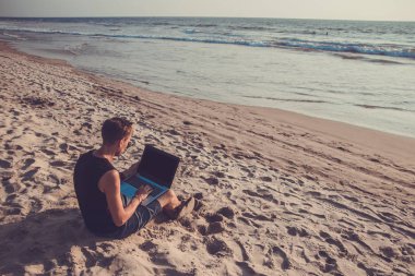 Genç adam sahilde dizüstü bilgisayar üzerinde çalışıyoruz. Ucu