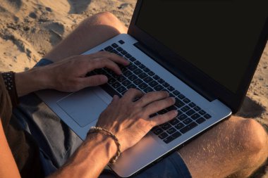 Genç adam sahilde dizüstü bilgisayar üzerinde çalışıyoruz. Ucu