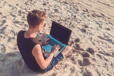 Genç adam sahilde dizüstü bilgisayar üzerinde çalışıyoruz. Ucu