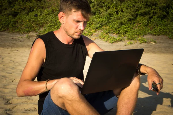 O jovem está a trabalhar num computador portátil na praia. Desfasamento — Fotografia de Stock