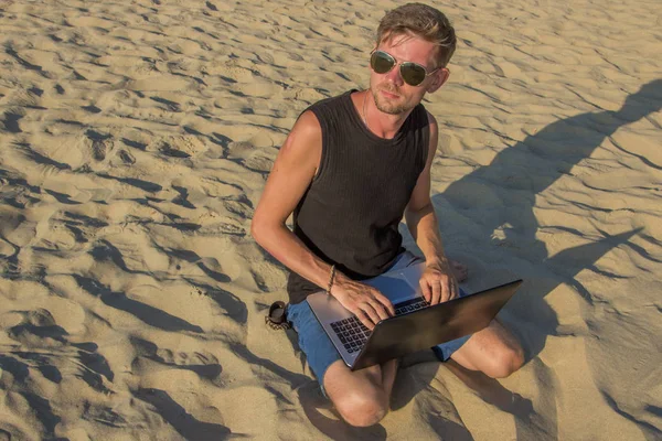 Genç adam sahilde dizüstü bilgisayar üzerinde çalışıyoruz. Ucu