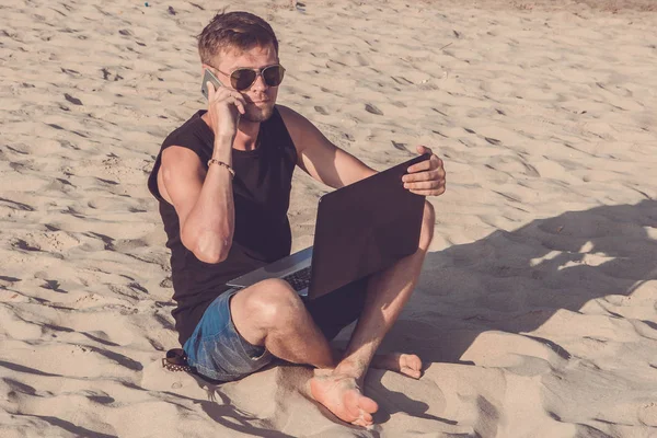 Mladý muž s přenosným počítačem a mobilní telefon na pláži. Atrakce — Stock fotografie