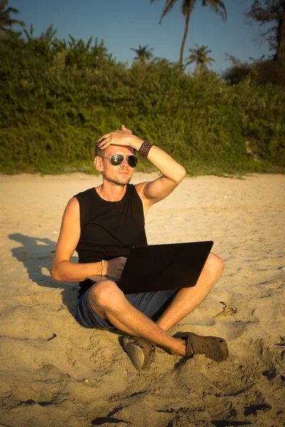 O jovem está a trabalhar num computador portátil na praia. Desfasamento — Fotografia de Stock