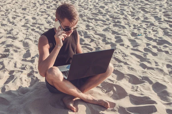 Un joven que trabaja en un ordenador portátil en la playa. Desplazamiento Imagen De Stock