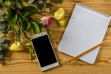 Smartphone, boş kağıt, kalem ve eustoma ahşap arka plan üzerinde