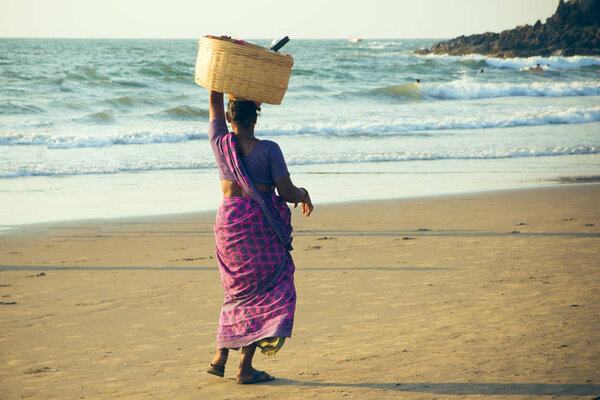 GOA, INDIA - MARCH 4: Woman in saris with basket on her head wal