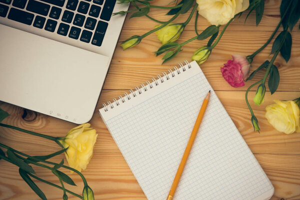 Laptop computer, blank paper, pencil and eustoma flowers on wood