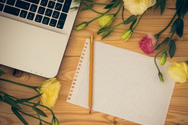 Dizüstü bilgisayar, boş kağıt, kalem ve eustoma çiçekler ahşap üzerine