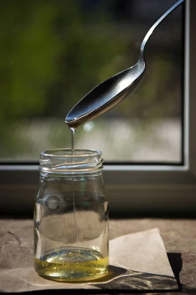 Βιολογικό αγνό μέλι σε βάζο στο περβάζι του παραθύρου. Ρεύμα του μελιού — Φωτογραφία Αρχείου