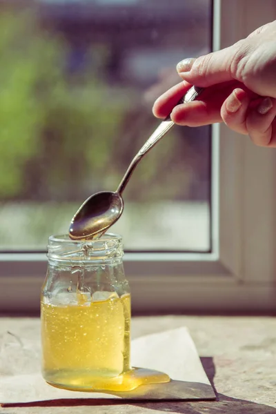 Miel goteando de una cuchara. Miel pura orgánica en frasco — Foto de Stock