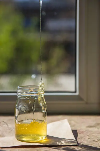 Orgánica miel pura en tarro en alféizar ventana. Corriente de miel — Foto de Stock