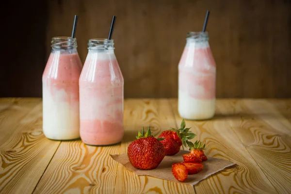 Smoothie s jahodou v lahvích na dřevěný stůl — Stock fotografie