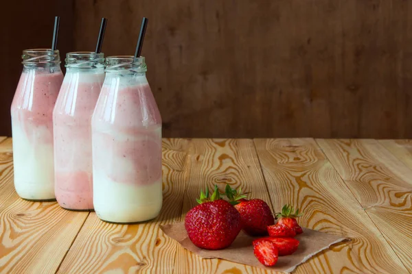 Smoothie s jahodou v lahvích na dřevěný stůl — Stock fotografie