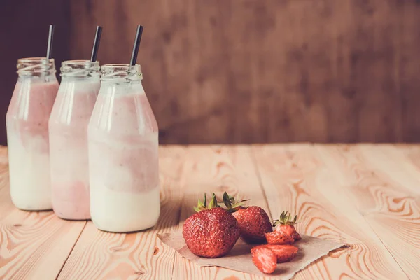 Smoothie s jahodou v lahvích na dřevěný stůl — Stock fotografie