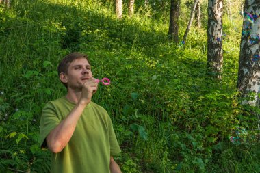Üfleme sabun köpüğü genç adam. Yarış yaz ormandaki adam