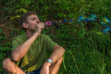 Üfleme sabun köpüğü genç adam. Yarış yaz ormandaki adam