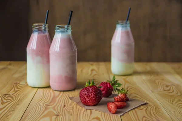 Smoothie s jahodou v lahvích na dřevěný stůl — Stock fotografie